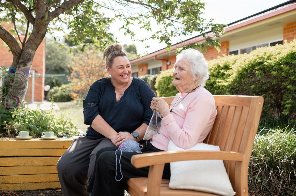 A carer and a resident sitting together on a garden bench